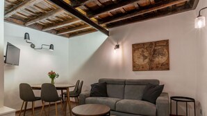 Un salon moderne avec un canapé gris, une table à manger en bois et des chaises. Une œuvre d'art représentant une carte est accrochée au mur, et il y a deux petites tables avec des télécommandes.
