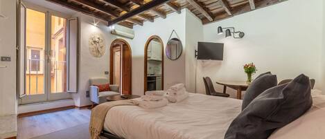 Habitación de hotel con cama, escritorio, silla, televisor y balcón.