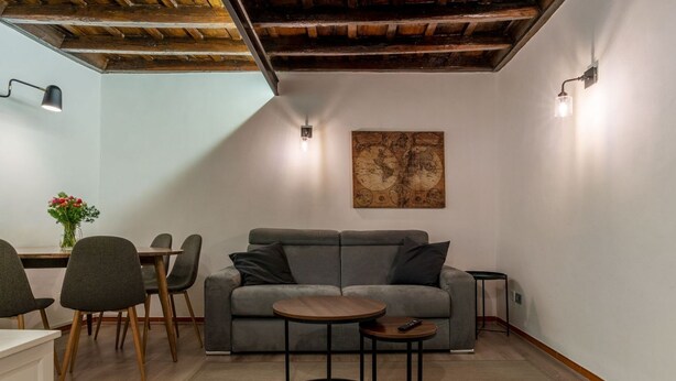 A cozy living room with a grey sofa, a small round table, and a dining area with chairs. - Quiet and cozy, by Campo de’ Fiori (Roma)