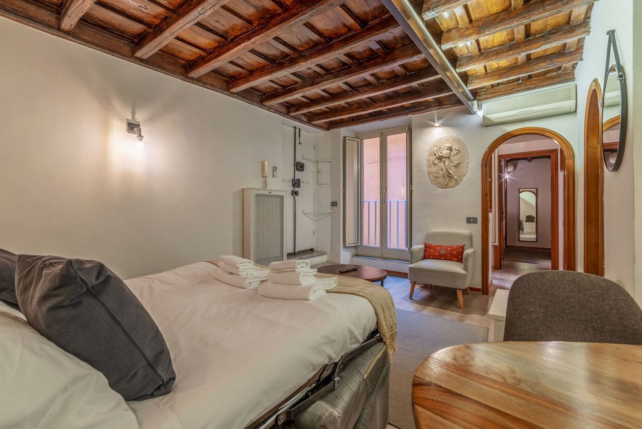 Un dormitorio con techo de madera, una cama con almohadas y toallas, una silla, una mesa y una puerta que da a otra habitación.