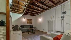 A modern living room with a wooden ceiling, a grey sofa, a small round table, and a white cabinet. - Quiet and cozy, by Campo de’ Fiori (Roma)