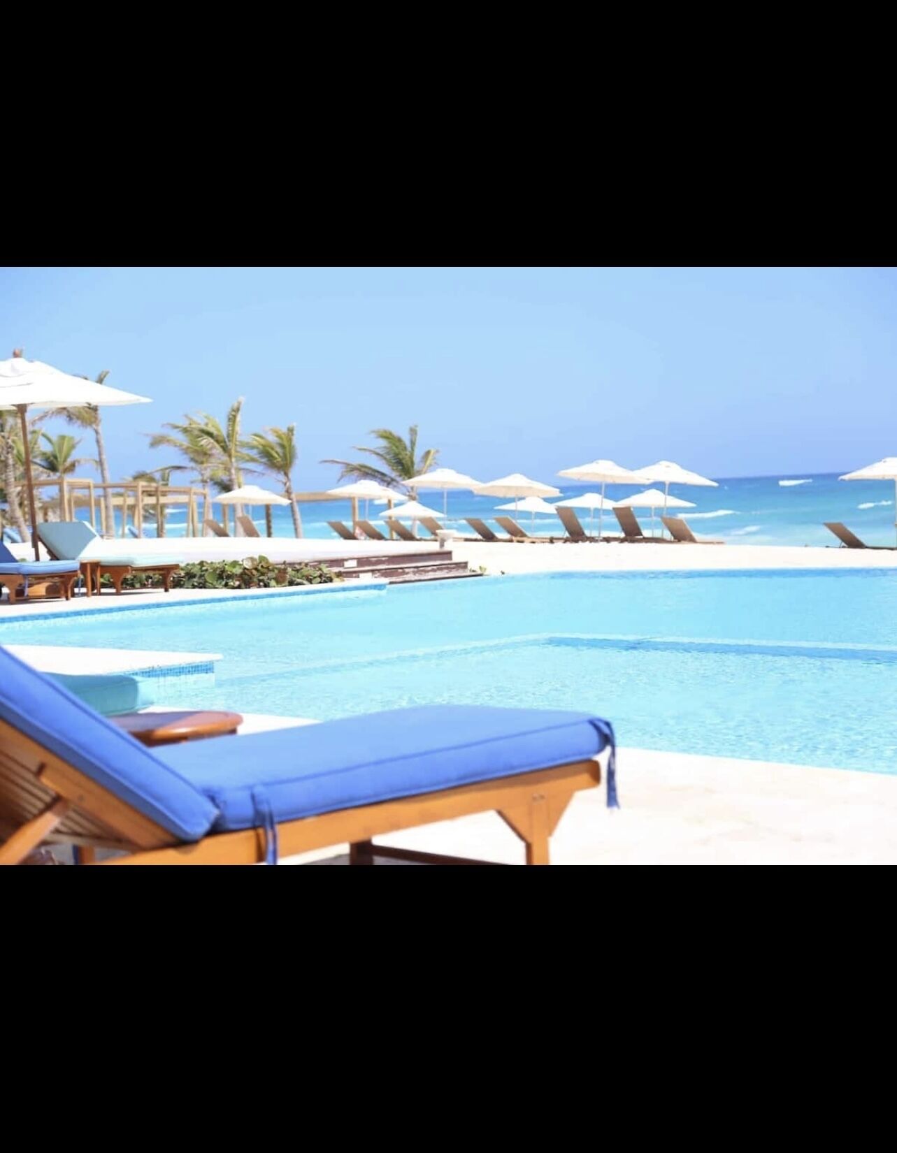 Área de piscina com espreguiçadeiras e guarda-sóis, com vista para um oceano azul e límpido.
