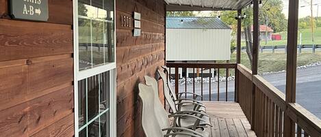 A wooden porch with a welcome sign, a window, and a row of white rocking chairs.