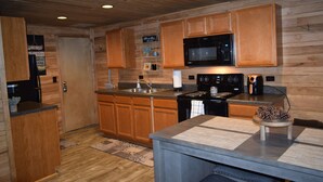 A wooden-paneled kitchen with a built-in microwave, stove, and sink. - Grand Rivers, KY - Unit A - Cozy getaway with Cabin Charm near KY & Barkley Lake (Grand Rivers)