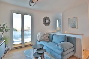 Uma sala de estar moderna com um sofá azul, uma mesinha de centro e uma grande janela com vista para um corpo d'água.