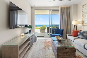 A modern hotel room with a large TV, a sofa, a coffee table, and a view of the ocean. - Luxury 2 bedroom condo with pool near Eagle Beach (Noord)