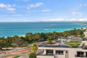 A coastal view with a beach, palm trees, and modern buildings. - Luxury 2 bedroom condo with pool near Eagle Beach (Noord)