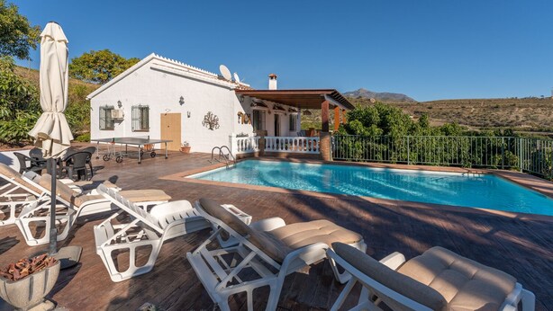 A pool area with lounge chairs, a pergola, and a white building with a mountain backdrop. - Villa Tropicana by Solset (Nerja)