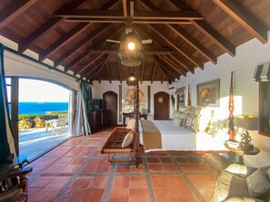 Enjoy ocean views from the large window in this room, featuring a comfortable bed and a decorative wall hanging.