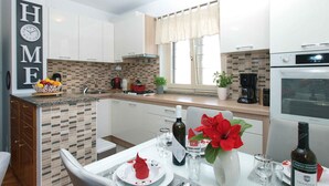 A modern kitchen with white cabinets, a tiled backsplash, and a dining area set with a table, chairs, and a vase of red flowers. - Holiday home mit Klimaanlage und Terrasse (Vinkuran)