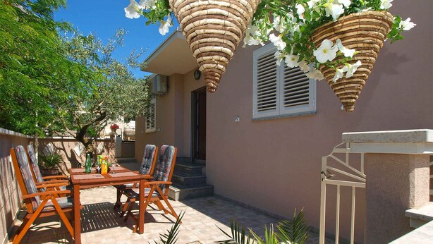 A patio with a wooden table and chairs, surrounded by potted plants and a hanging basket with flowers. - Holiday home mit Klimaanlage und Terrasse (Vinkuran)
