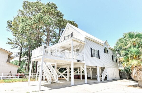 A white two-story house with a balcony, a covered porch, and a palm tree in the background. - 1 block to beach Pet friendly large deck & living space +plenty PK (Surfside Beach)