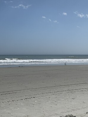 A beach with a clear sky, waves, and a distant person running. - 1 block to beach Pet friendly large deck & living space +plenty PK (Surfside Beach)