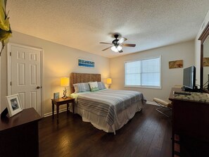 A bedroom with a bed, two bedside tables, a ceiling fan, a window with blinds, a dresser, and a television. - 1 block to beach Pet friendly large deck & living space +plenty PK (Surfside Beach)