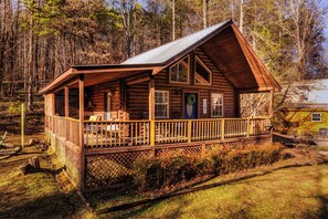 A log cabin with a porch, a door with a wreath, and a window with a view of the forest.