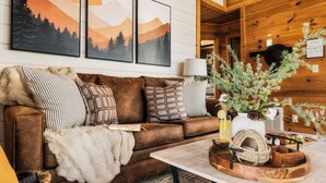 A cozy living room with a brown leather couch, patterned pillows, a white fur throw, a wooden coffee table with a woven basket, and a vase with greenery. - ☆Renovated Cabin☆ Hot Tub ◇ Fire Pit ◇ Fireplace ◇ Dog-friendly (Sevierville)