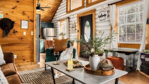 A cozy cabin interior with a wooden interior, a dining table with a pitcher and snacks, a sofa, and a window with curtains. - ☆Renovated Cabin☆ Hot Tub ◇ Fire Pit ◇ Fireplace ◇ Dog-friendly (Sevierville)