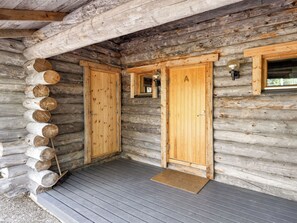 Eine Blockhütte mit zwei Holztüren, einer Veranda und einem Fenster mit einer Lampe.