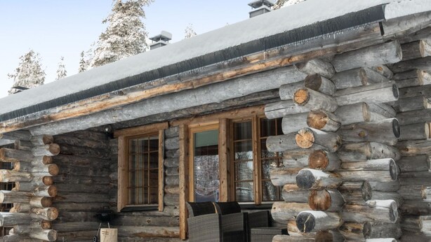 Een vakantiehuisje van hout met een veranda, grote ramen en een sneeuwbedekte dak.