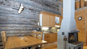 Een houten interieur met een eettafel, stoelen, een keuken met houten kasten en een houtkachel.