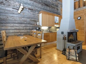 Ein Holzinnenraum mit Esstisch, Stühlen, einer Küchenzeile mit Holzschränken und einem Kaminofen.