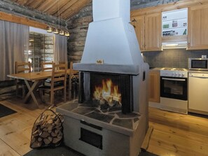 A rustic kitchen with a stone stove, wooden cabinets, and a dining area with a table and chairs.