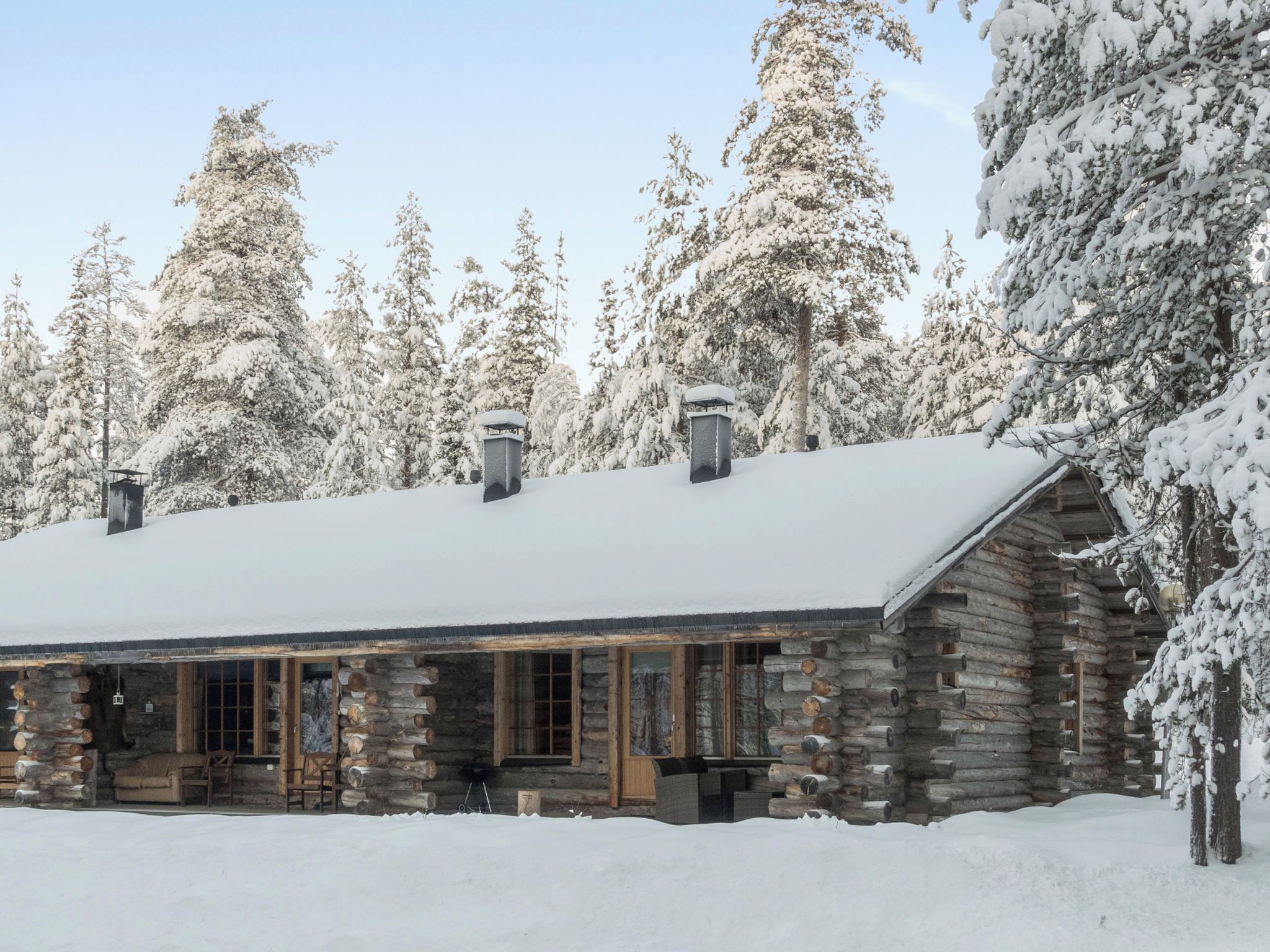 A log cabin with a snow-covered roof, surrounded by snow-laden trees.