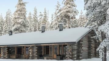 A log cabin with a snow-covered roof, surrounded by snow-laden trees.