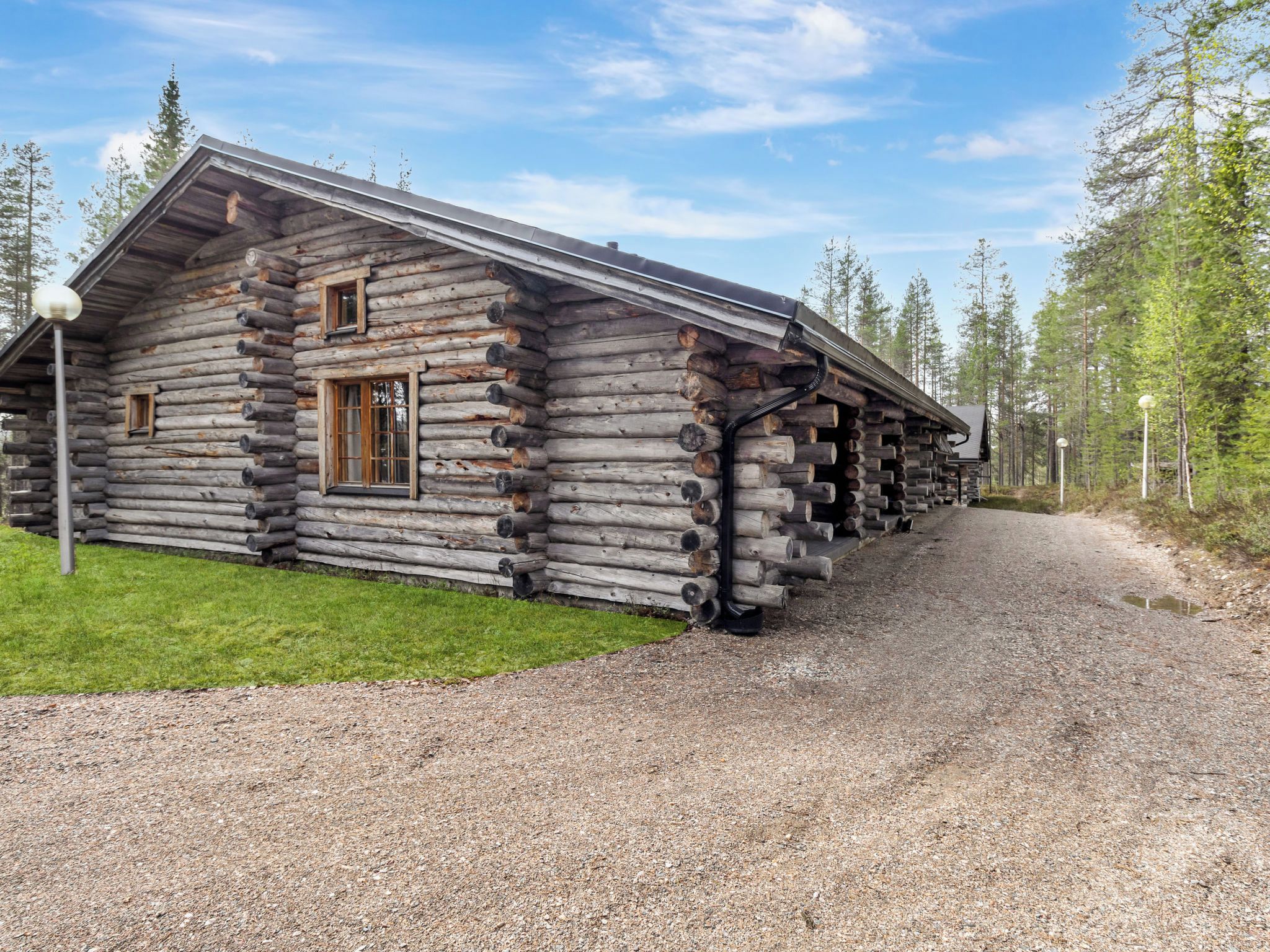 A log cabin with a gravel driveway and a forested area in the background.
