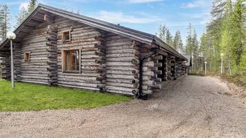 A log cabin with a gravel driveway and a forested area in the background.