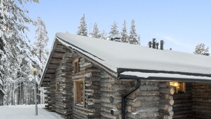 Een blokhut met een sneeuwbedekte dak, een houten deur en een klein terras.