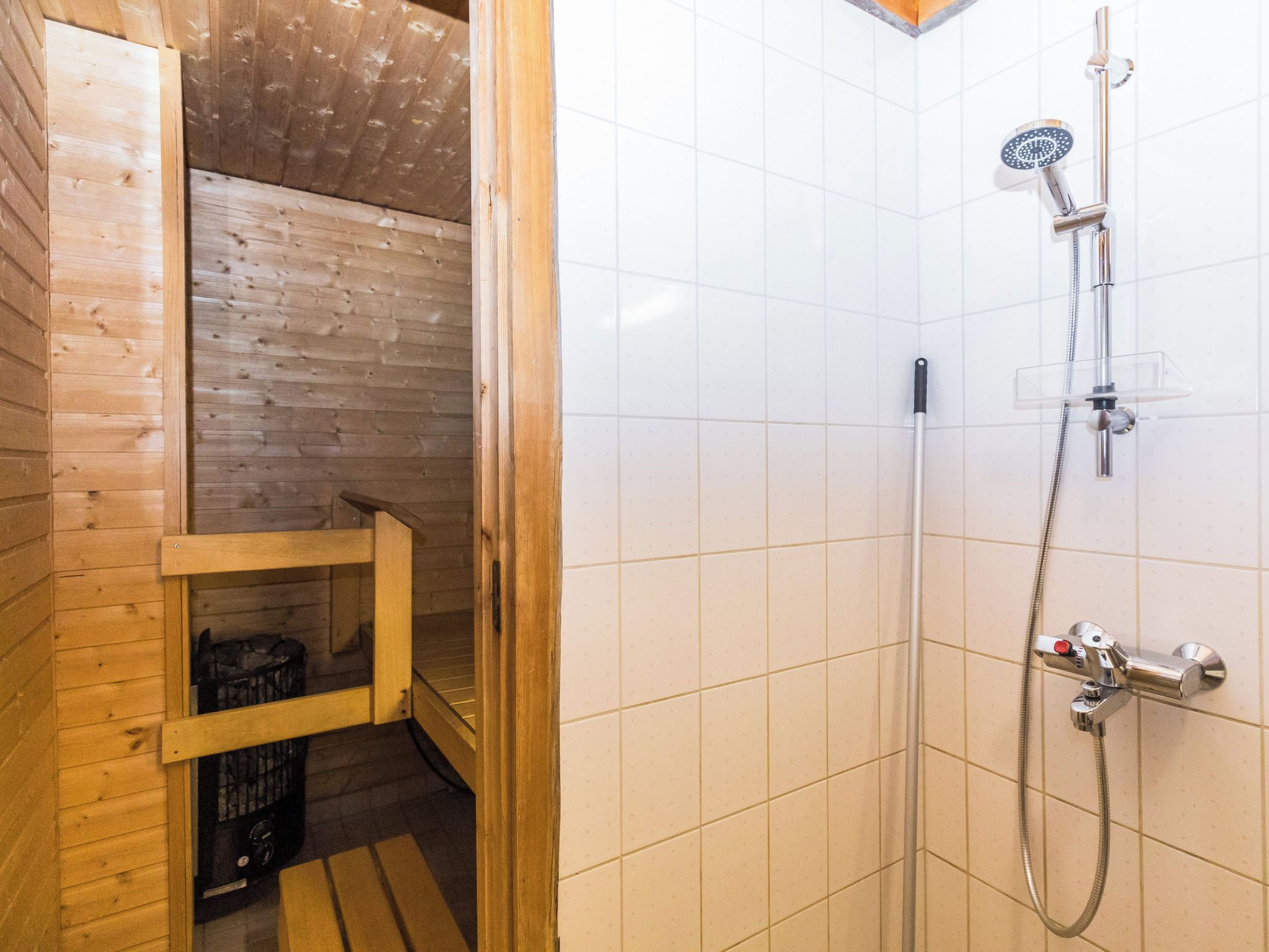 Ein Saunaraum mit einer hölzernen Sitzbank, einem Duschbereich mit Handbrause und einer gefliesten Wand.