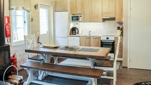 Cocina compacta con armarios de madera, microondas, cafetera y estufa. Hay una mesa con bancos y un extintor cerca de la entrada.
