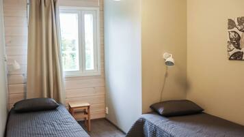 A room with two beds, a window with curtains, a small table, a wall-mounted lamp, and a wall art piece.