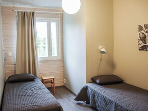 Una habitación con dos camas, una ventana con cortinas, una mesita, una lámpara de pared y una obra de arte en la pared.