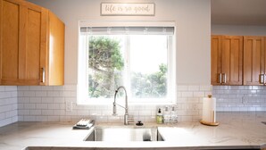 A kitchen with wooden cabinets, a white countertop, a stainless steel sink, and a window with a view of trees. - Family and pet friendly! 4 Bd, 3 bath beach house with ocean views! Sleeps 10! (Rockaway Beach)
