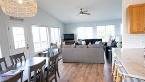 A spacious living area with a sofa, dining table, and chairs, a kitchen with a bar, and large windows. - Family and pet friendly! 4 Bd, 3 bath beach house with ocean views! Sleeps 10! (Rockaway Beach)