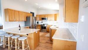 A modern kitchen with wooden cabinets, stainless steel appliances, and a central island with bar stools. - Family and pet friendly! 4 Bd, 3 bath beach house with ocean views! Sleeps 10! (Rockaway Beach)