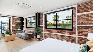 Une chambre d’hôtel moderne avec un grand lit, un canapé gris, une petite table ronde et un mur en briques.