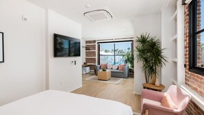 Una habitación de hotel moderna con una cama grande, un área de estar con un sofá y sillones, una mesita y un ventanal con vistas a palmeras.