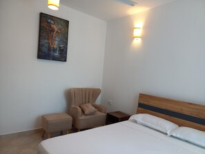 A hotel room with a bed, a chair, a small table, and a painting on the wall.