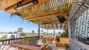 Una terraza en la azotea con mobiliario de madera, plantas colgantes y baldosas estampadas.