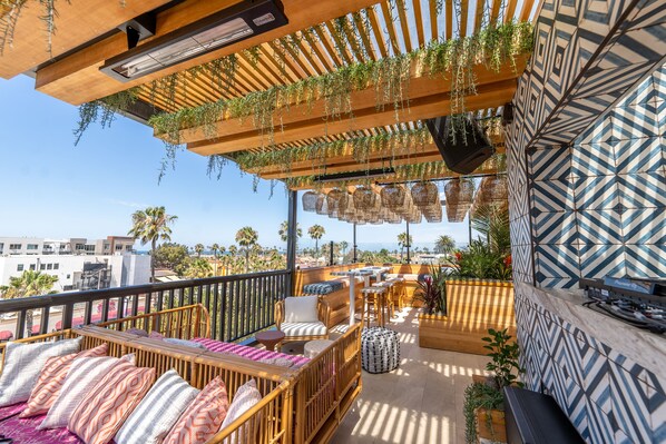 Una terraza en la azotea con mobiliario de madera, plantas colgantes y baldosas estampadas.