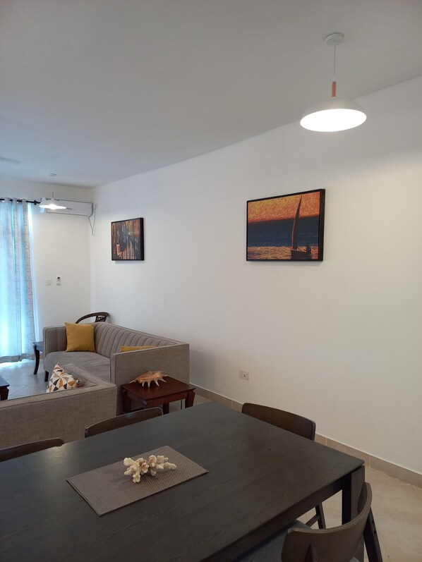 A modern living room with a sofa, a dining table, and two paintings on the wall.