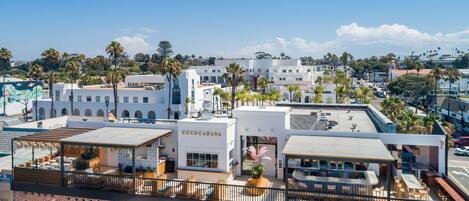 A rooftop bar with outdoor seating, a white building with "COCOCABANA" signage, and a view of palm trees and other buildings in the background.