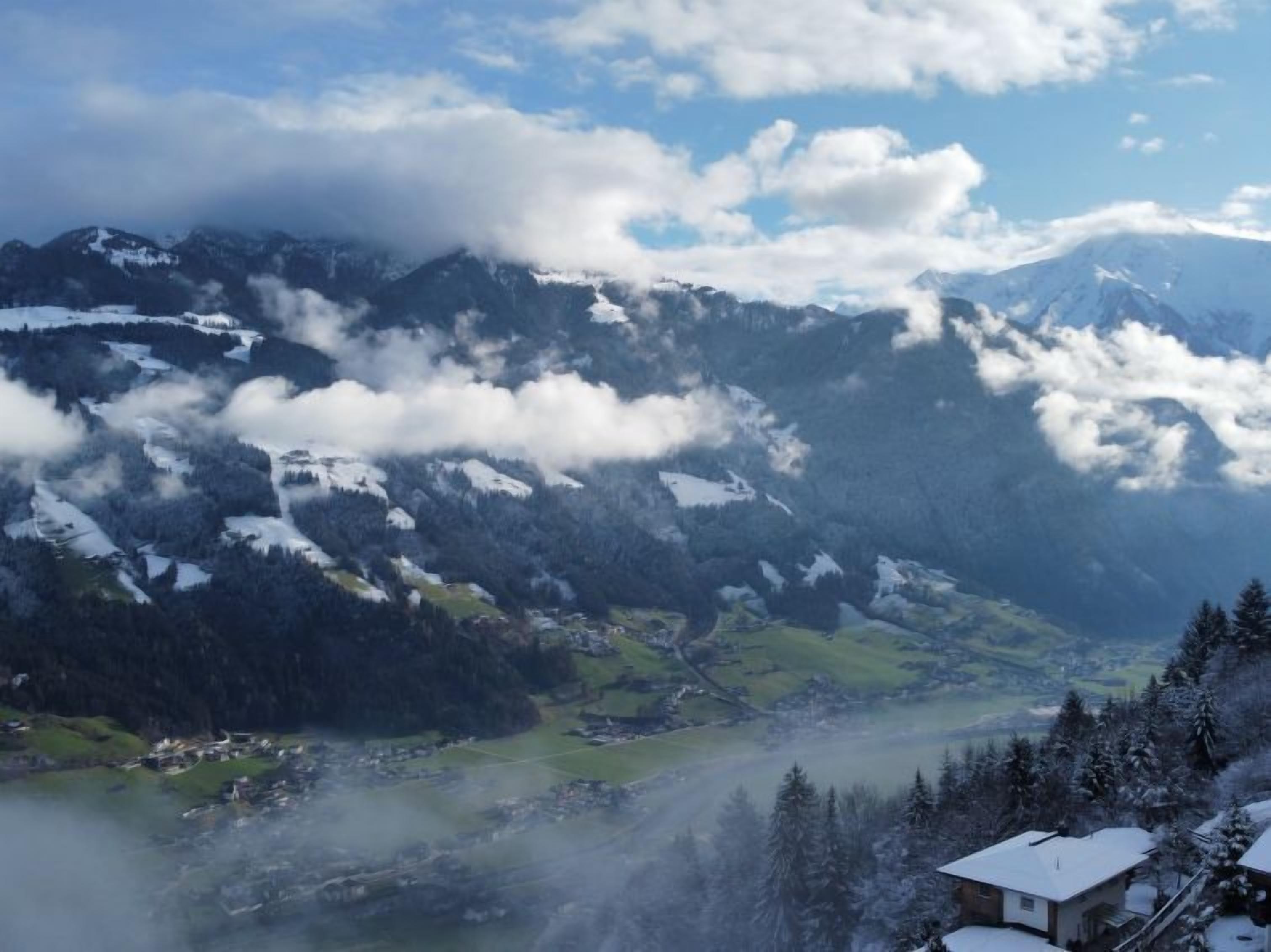 Eine gebirgige Landschaft mit schneebedeckten Gipfeln, einem Tal mit Gebäuden und einem Haus mit verschneitem Dach.
