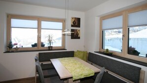 A dining area with a table and benches, large windows with blinds, and a view of a snowy landscape. - Apartment Nina by Interhome (Hippach)