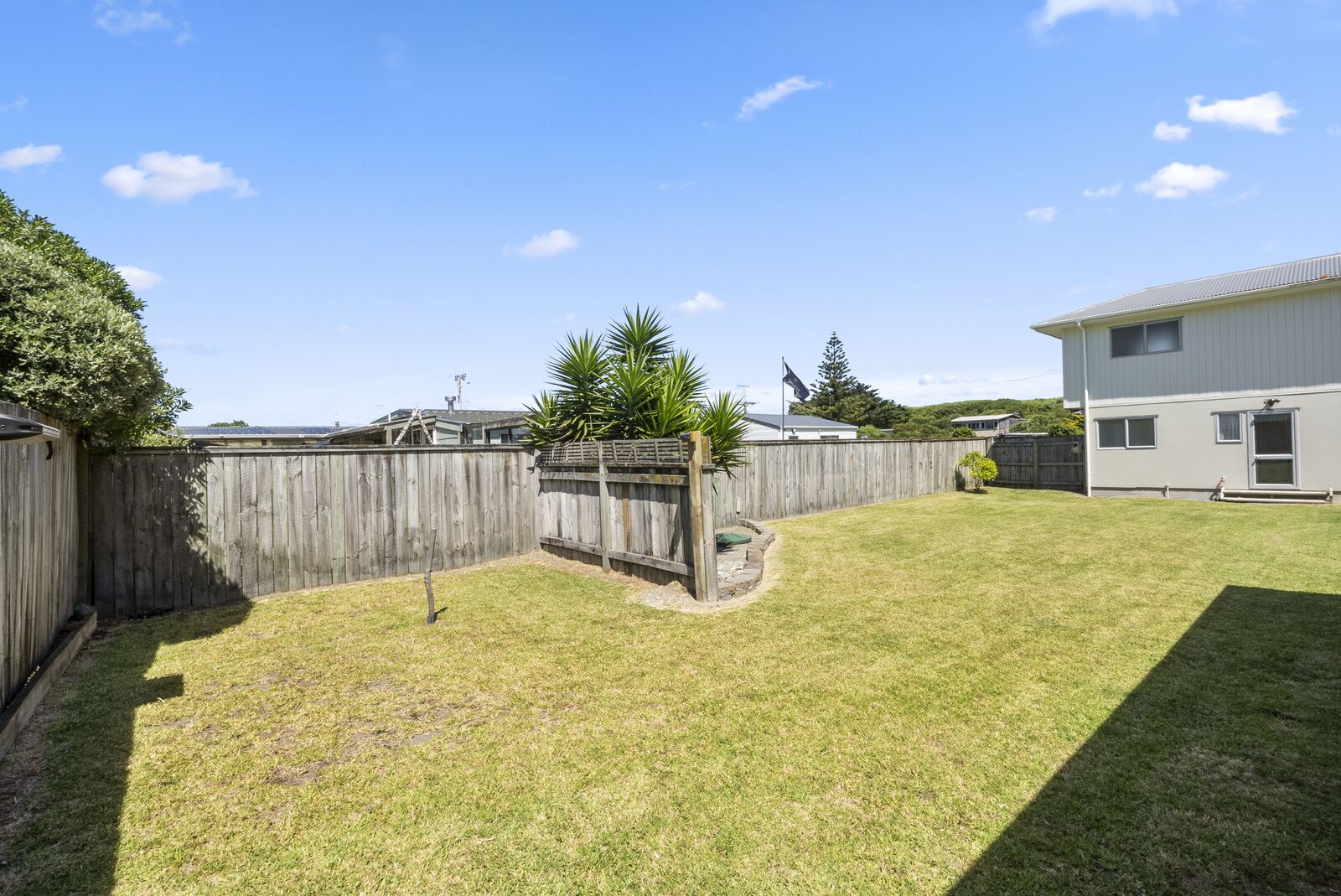 A backyard with a wooden fence, a grassy lawn, and a house with a metal roof.