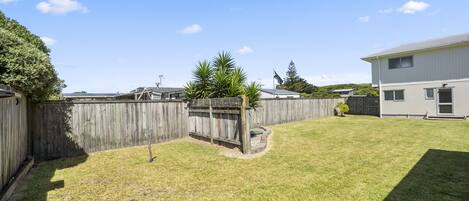 A backyard with a wooden fence, a grassy lawn, and a house with a metal roof.