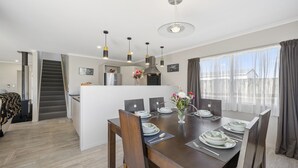 Une cuisine moderne dotée d’un îlot central, d’un coin repas avec une table en bois prévue pour quatre personnes, et d’un escalier menant à un autre niveau.